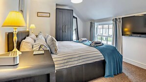 Une chambre d’hôtel avec un lit, des lampes de chevet, un bureau avec un téléphone, un téléviseur fixé au mur et une fenêtre avec des rideaux.