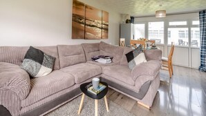 Uma sala de estar com um amplo sofá modular, uma mesa de centro e um espaço de jantar com mesa e cadeiras.