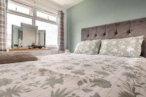 A bedroom with a bed, a dresser, a mirror, and a window with curtains. - 2 Bed in Freshwater East (oc-91445) (Freshwater East)