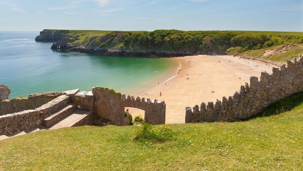 Uma praia costeira com um muro de pedra e escadas que descem até a água.