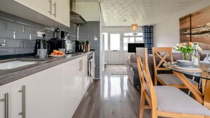 Uma cozinha moderna com armários brancos, bancada de madeira e um espaço de jantar com mesa de vidro e cadeiras de madeira.