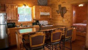 Interior de una cabaña de madera con cocina, comedor y una cama.
