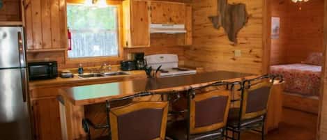 Interior de una cabaña de madera con cocina, comedor y una cama.