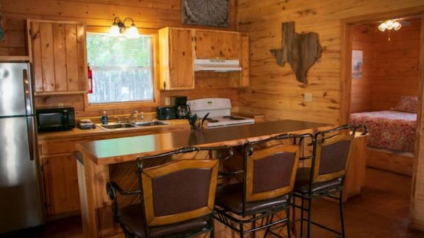 Interior de una cabaña de madera con cocina, comedor y una cama.