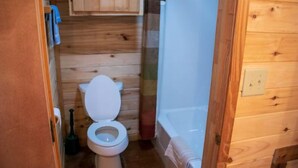Baño de cabaña de madera con inodoro, piso de madera y un interruptor de luz a la vista.