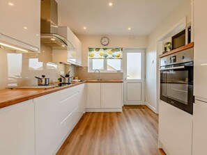 A modern kitchen with white cabinets, a wooden countertop, a built-in oven, and a clock on the wall. - 3 Bed in Swanage (oc-91451) (Swanage)
