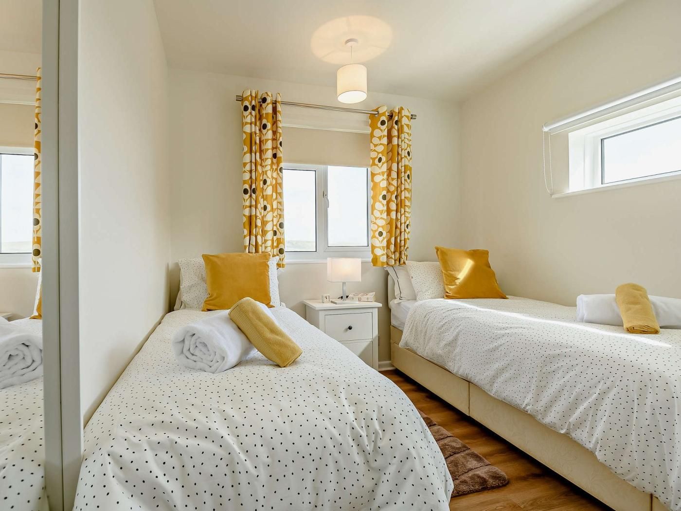 A bedroom with two beds, a nightstand, a lamp, and a window with curtains.