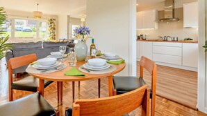 Een eetgedeelte met een ronde tafel voor vier personen, een bankstel op de achtergrond en een keuken zichtbaar door een open doorgang.