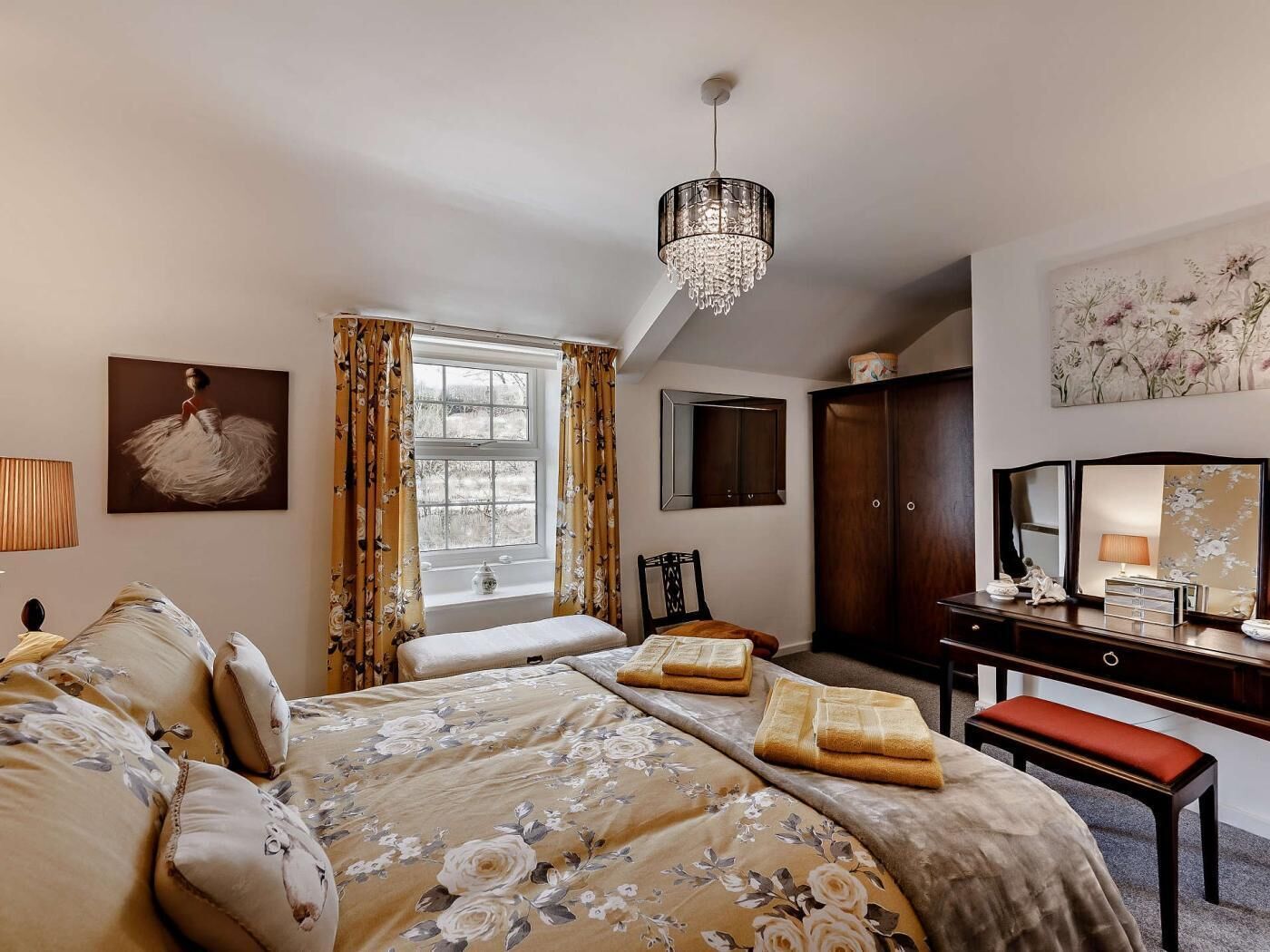 A bedroom with a bed, a desk, a chair, a wardrobe, a chandelier, and a window with curtains.