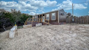 A wooden cabin with a porch, a fenced yard, and a clear sky. - Riverfront Cabins  and  Vacation Homes (Rio Frio)
