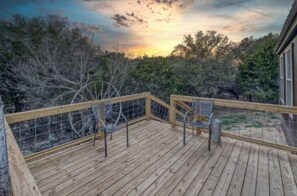 Eine Holzterrasse mit Stühlen und Geländer, mit Blick auf eine natürliche Landschaft mit Bäumen und Sonnenuntergang.