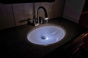 Ein Waschtisch mit Wasserhahn, ein Spiegel darüber und eine Steckdose an der Wand.