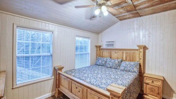 A bedroom with a wooden bed, two windows with blinds, a ceiling fan, and built-in wooden cabinets. - Riverfront Cabins  and  Vacation Homes (Rio Frio)