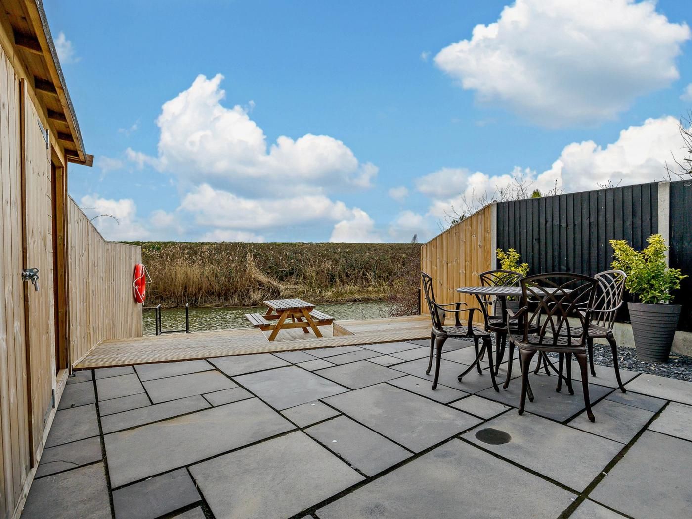 A patio with a table and chairs, a wooden fence, and a view of a water body.