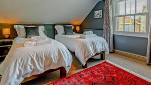 Um quarto com duas camas, um tapete vermelho estampado e uma janela com cortinas.
