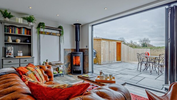 Uma sala de estar moderna com um sofá de couro, estante, lareira e área de varanda com móveis de exterior.