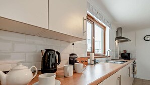 Et moderne køkken med hvide skabe, en træbordplade, kaffemaskine, elkedel og et ur på væggen.