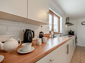 Eine moderne Küche mit weißen Schränken, einer Holzarbeitsplatte, einer Kaffeemaschine, einem Wasserkocher und einer Uhr an der Wand.