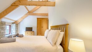 A bedroom with a wooden ceiling, a bed with white bedding, a nightstand with a lamp, a wooden wardrobe, and a television on a dresser. - 3 Bed in Tenby (oc-91524) (Sageston)
