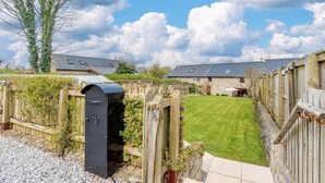 A residential property with a well-maintained lawn, a wooden fence, and a stone building with a sloped roof. - 3 Bed in Tenby (oc-91524) (Sageston)