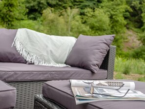 Ein Korbsessel mit Kissen und einer Decke, eine Brille und eine Zeitschrift auf einem Tisch.