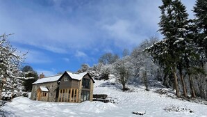 Une maison en pierre avec un toit à pignon, entourée d’arbres couverts de neige et sous un ciel dégagé.
