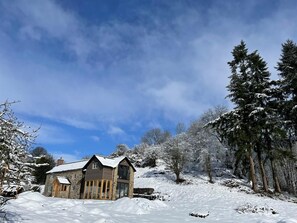 Ein Haus aus Stein mit einem Satteldach, umgeben von schneebedeckten Bäumen und einem klaren Himmel.