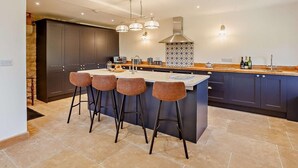 A modern kitchen with dark cabinets, a central island with bar stools, pendant lighting, and a patterned backsplash. - 4 Bed in Shaftesbury (oc-91456) (East Melbury)