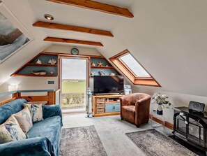 Une chambre confortable aménagée en mezzanine, avec un plafond en pente, une télévision, un fauteuil confortable et une vue sur l’extérieur.