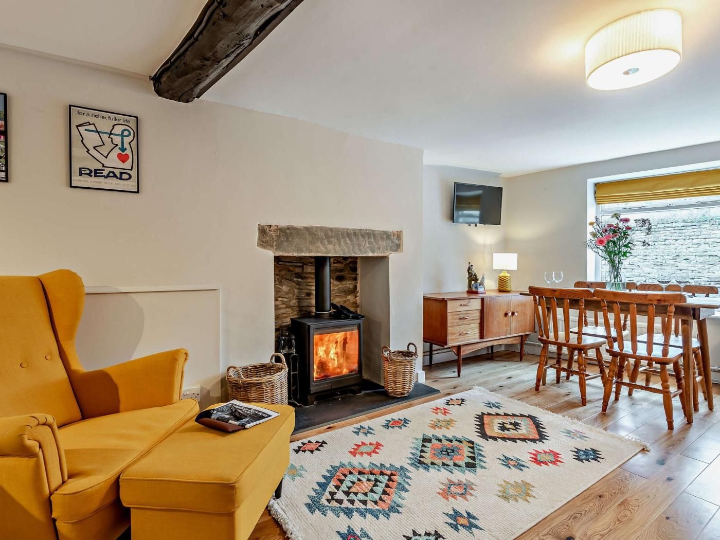 A cozy living room with a sofa, a fireplace, a dining area with chairs, a TV mounted on the wall, and a window with a view.