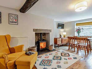 A cozy living room with a sofa, a fireplace, a dining area with chairs, a TV mounted on the wall, and a window with a view.