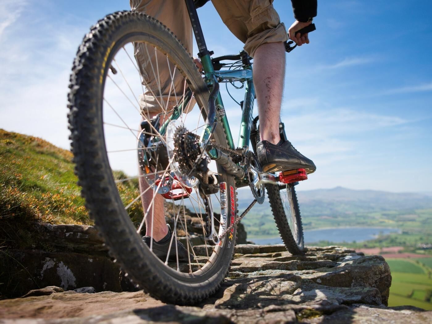 A mountain bike on a rocky path with a scenic view of green fields and distant mountains.