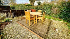 A patio with a wooden table and chairs, surrounded by a gravel area and dense foliage.