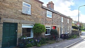 A stone-built residential street with a green door, a small garden with flowers, and a school crossing sign.