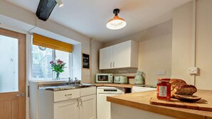 A compact kitchen with white cabinets, a wooden countertop, a sink, a microwave, a toaster, and a window with a yellow blind.