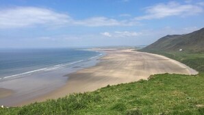 Paisagem costeira com uma praia, colinas gramadas e céu claro.