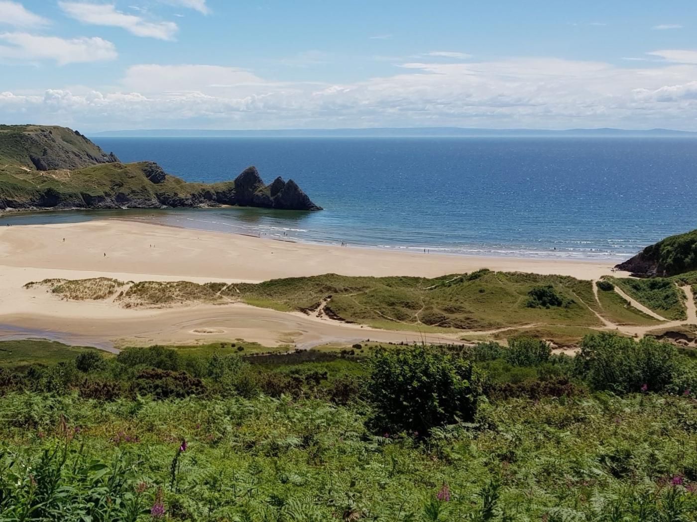 A coastal landscape with a sandy beach, grassy hills, and a clear view of the ocean.