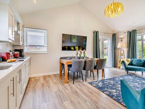 A modern kitchen with a dining area, a flat-screen TV, and a cozy seating area with a blue sofa.