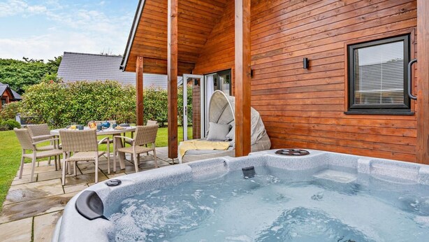 Uma cabana de madeira com banheira de hidromassagem, área de estar externa e um pátio coberto.