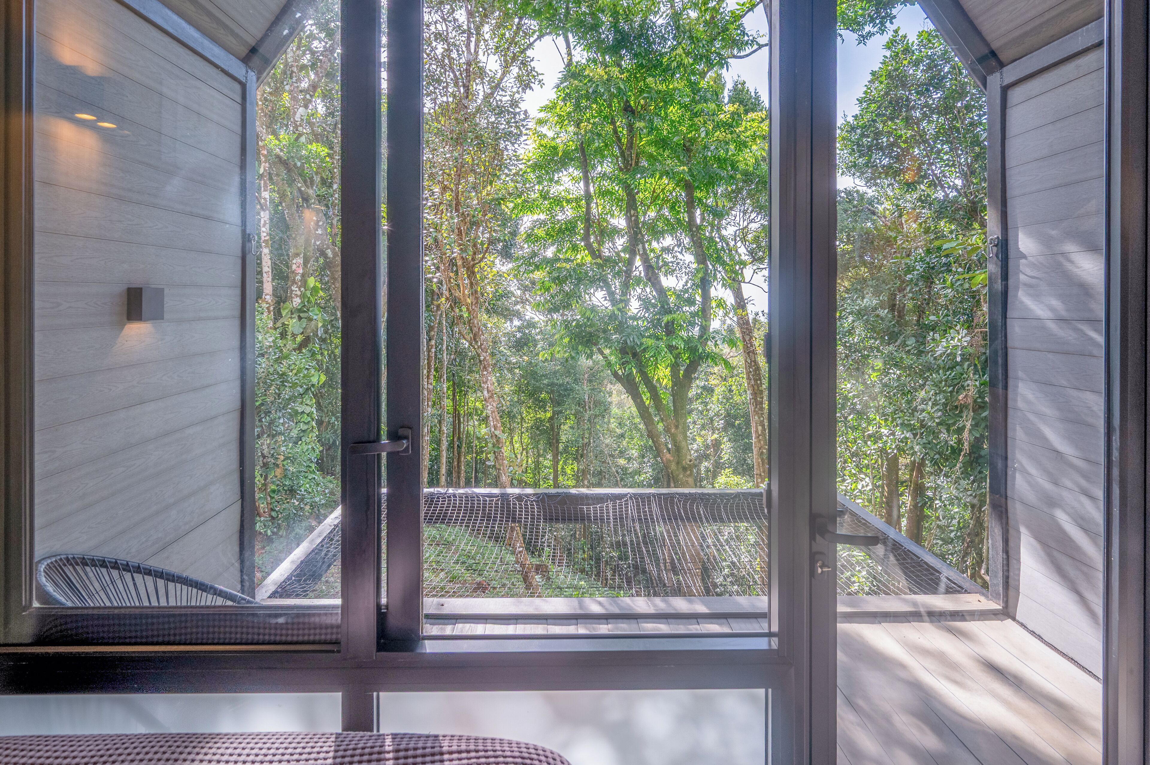 A room with a large window, a chair, and a view of a forest.