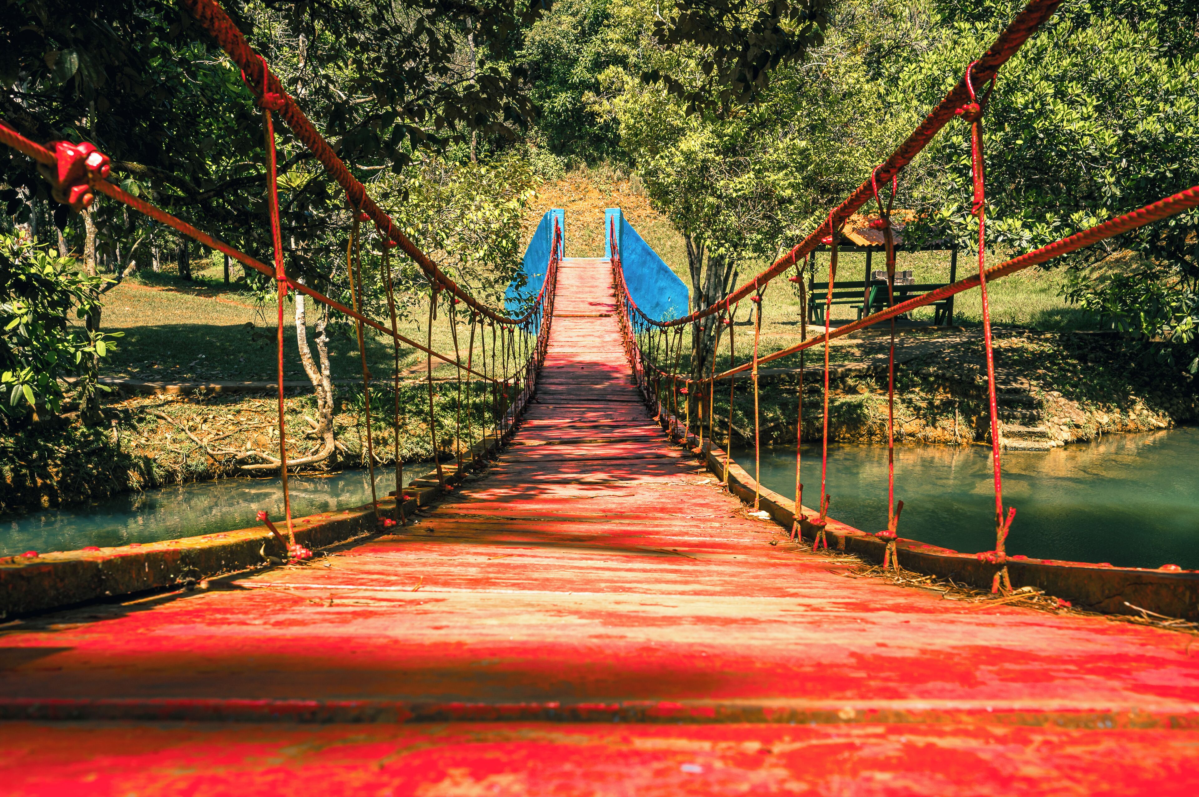 A suspension bridge with a red pathway leading to a blue structure at the end.
