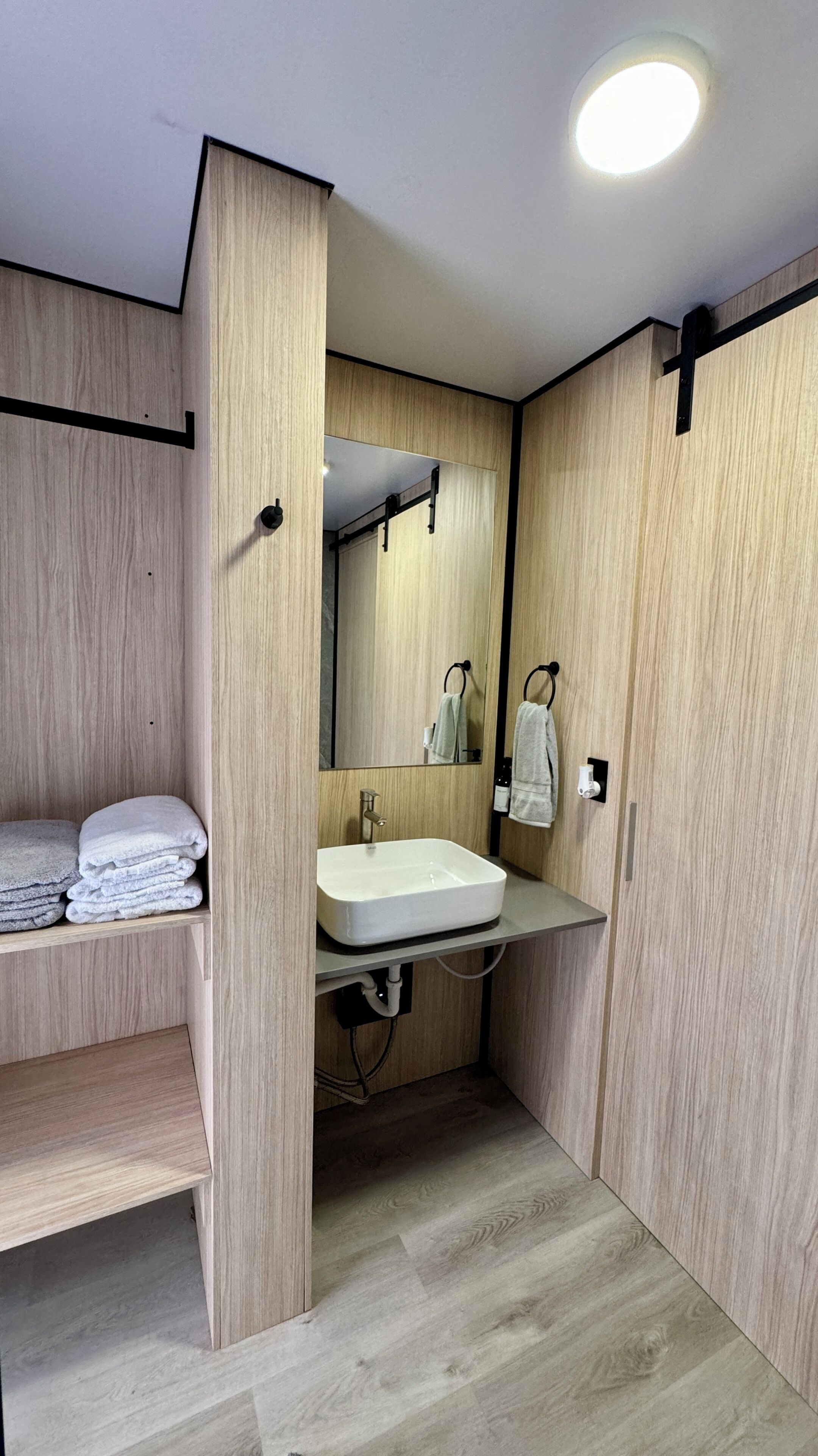 A compact bathroom with a built-in sink, a mirror, and a shelf with folded towels.