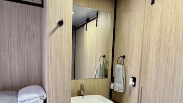 A compact bathroom with a built-in sink, a mirror, and a shelf with folded towels.
