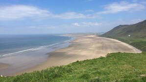 Eine Küstenlandschaft mit Strand, sanften Hügeln und blauem Himmel.