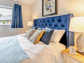 A bedroom with a tufted headboard, a bed with patterned pillows, a bedside table with a lamp, and a framed botanical print on the wall. - 2 Bed in Swansea (oc-91724) (Upper Killay)
