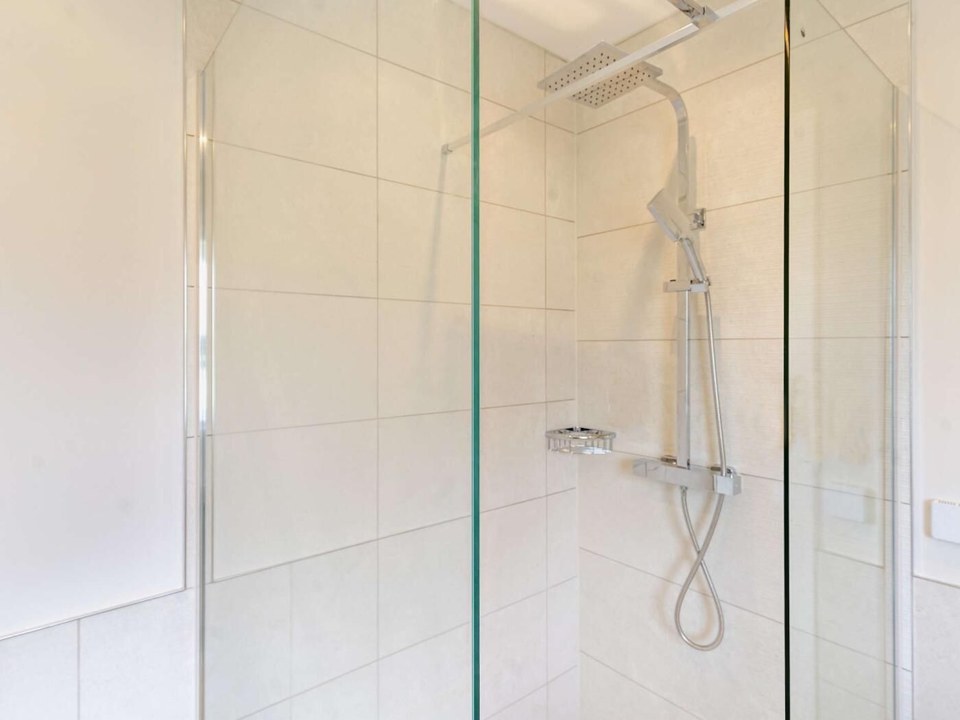 Une douche moderne dotée d’un pommeau de douche à main et d’un panneau de commande fixé au mur.