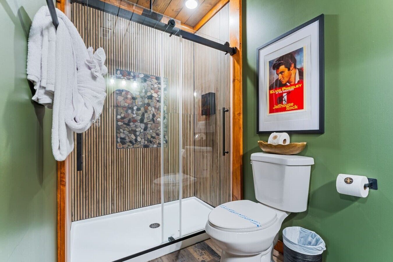 A bathroom with a shower enclosure, toilet, and a framed poster on the wall.