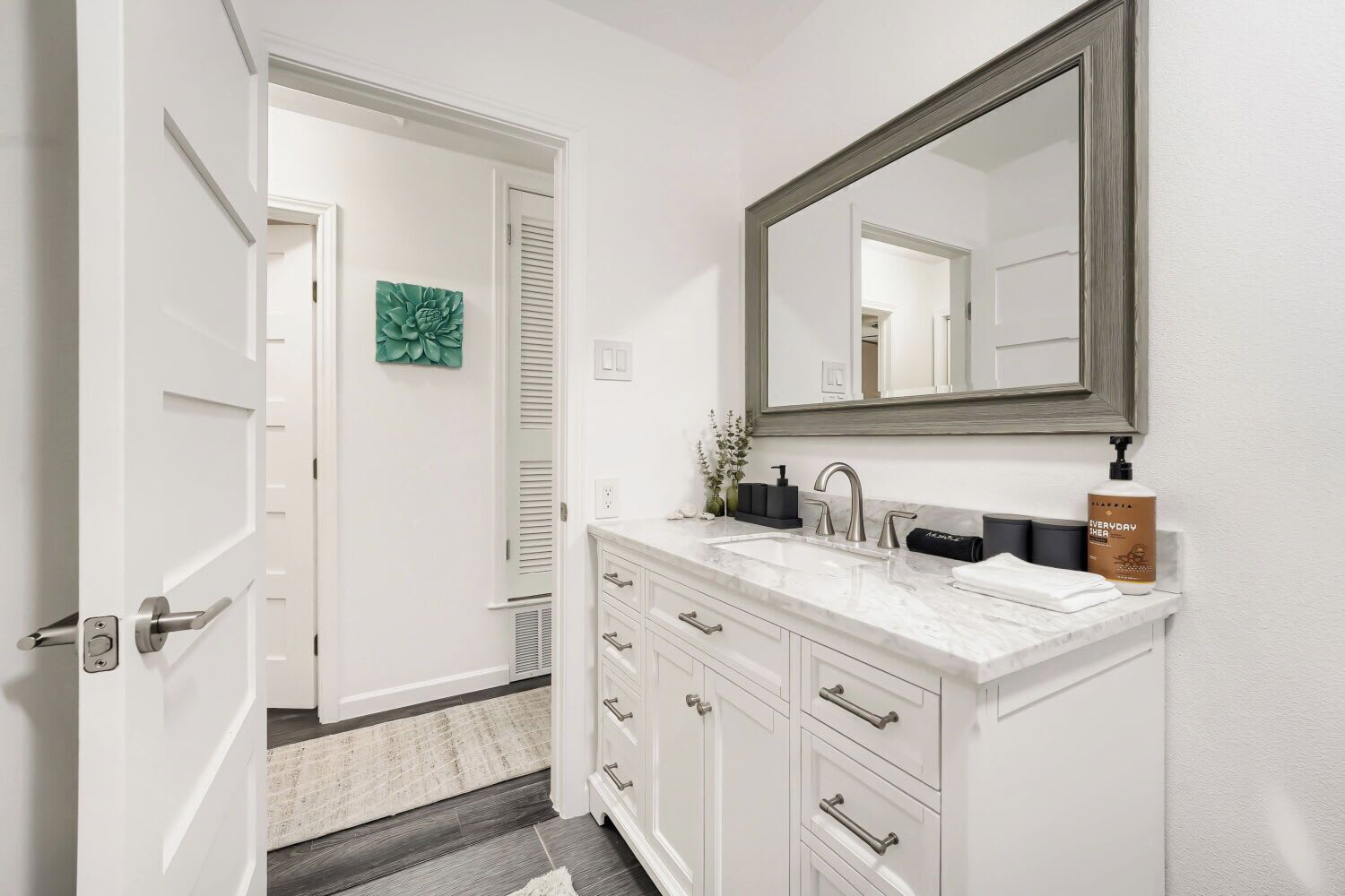 A bathroom with a white vanity, a large mirror, a sink, and a bottle of shampoo.