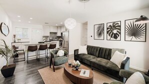 Un soggiorno moderno con divano, tavolino e poltrone. Si nota una cucina sullo sfondo con mobili bianchi e un'area pranzo con sgabelli da bar.