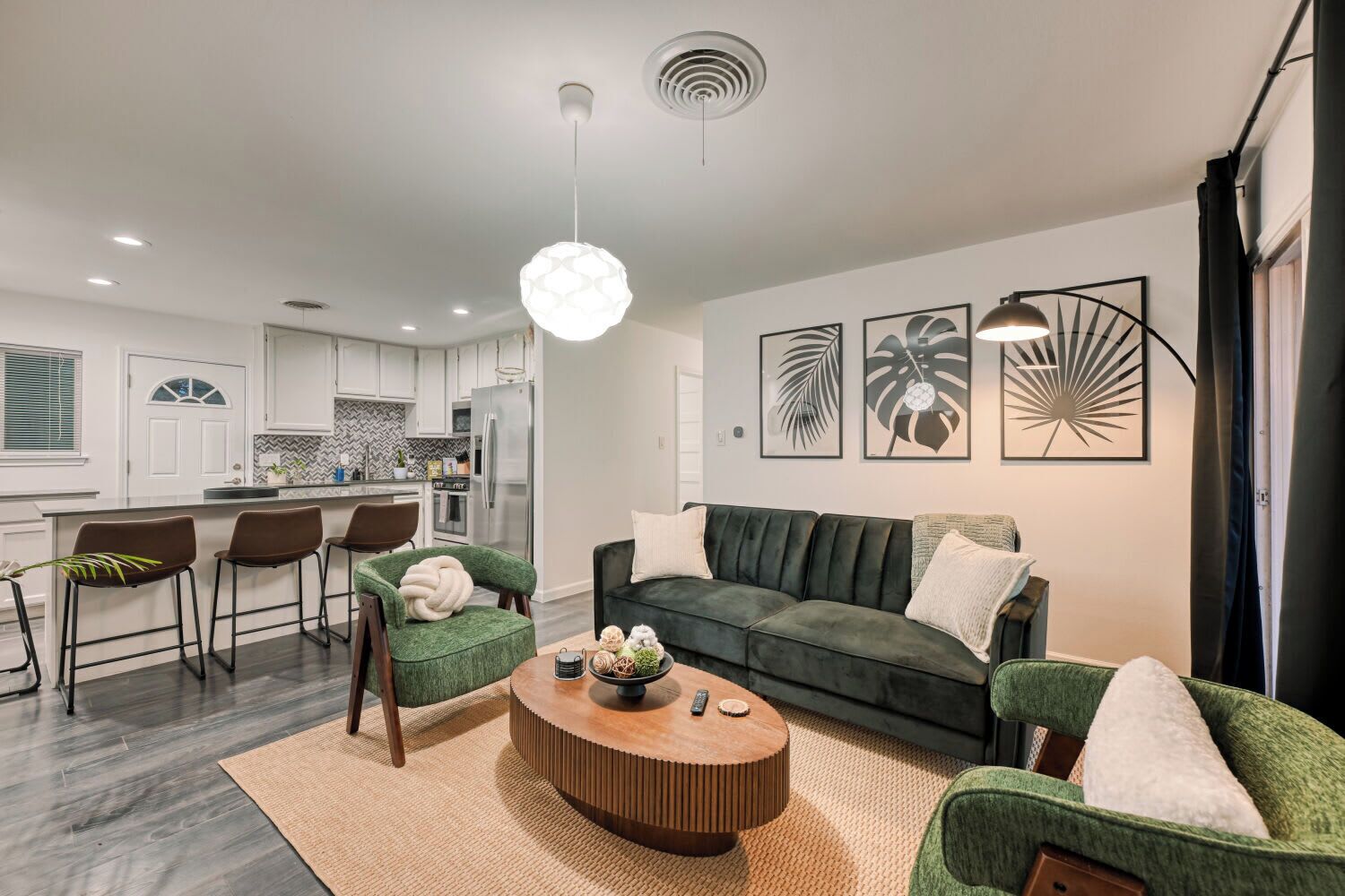 A modern living room with a green sofa, matching armchairs, a wooden coffee table, and a kitchen in the background.